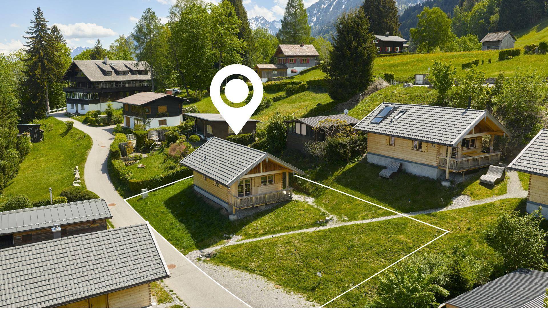 Vogelperspektive eines Holzchalets mit Grundstück in einer idyllischen Bergregion.
