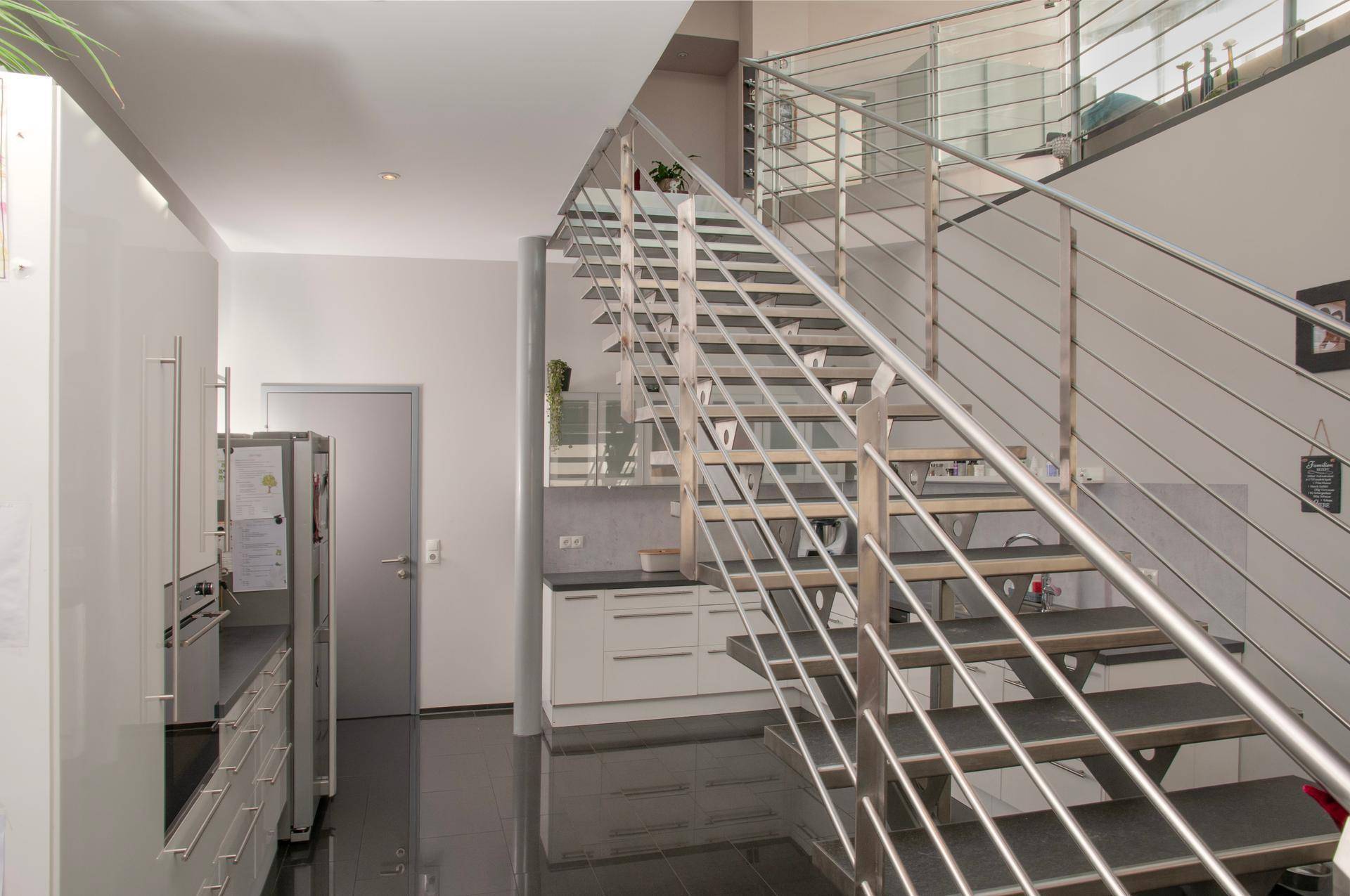 Moderne Küche mit weißen Schränken und offener Treppe, die zum oberen Wohnbereich führt.