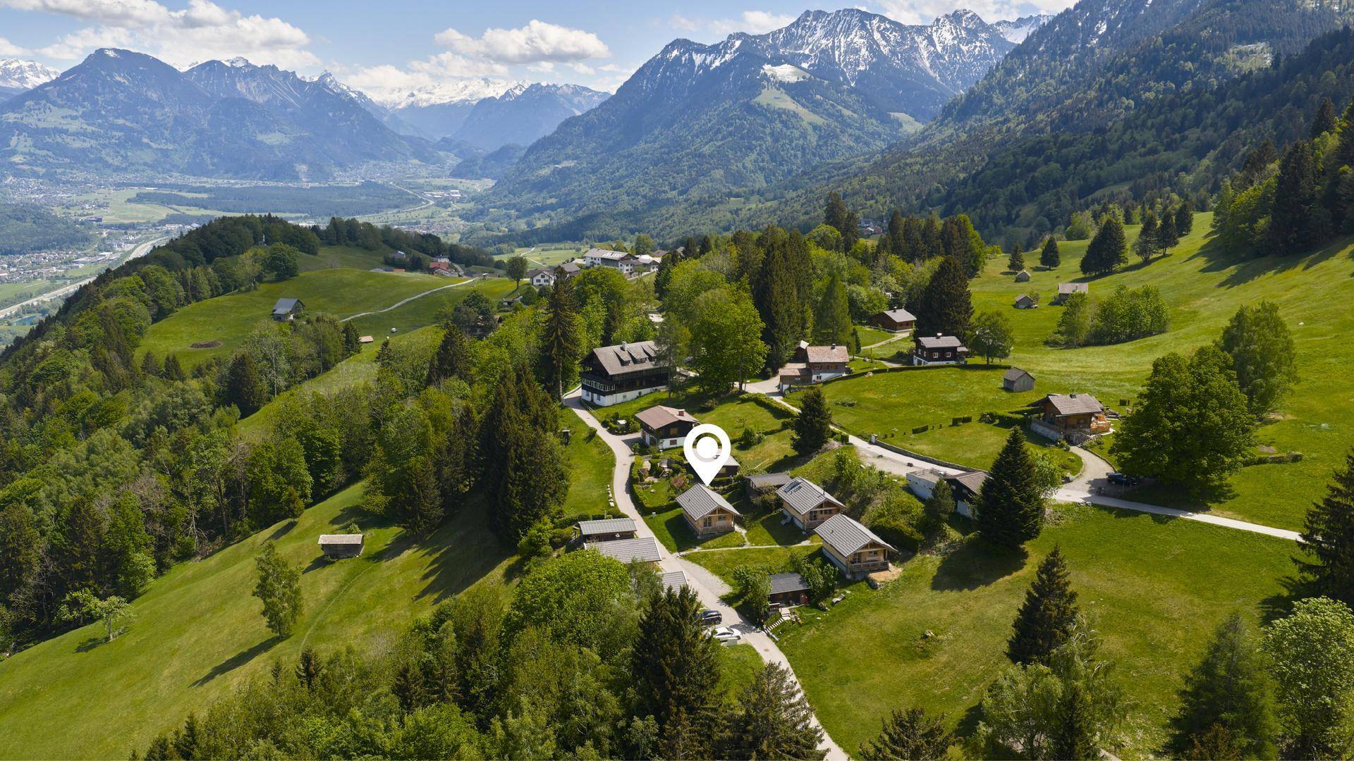 Luftaufnahme einer Siedlung von Holzchalets in einer malerischen Berglandschaft.