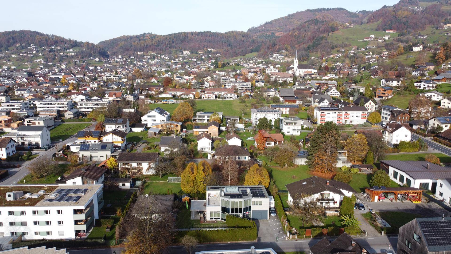 Weitläufige Luftaufnahme einer Wohnsiedlung mit vielen Häusern und grünen Hügeln im Hintergrund.