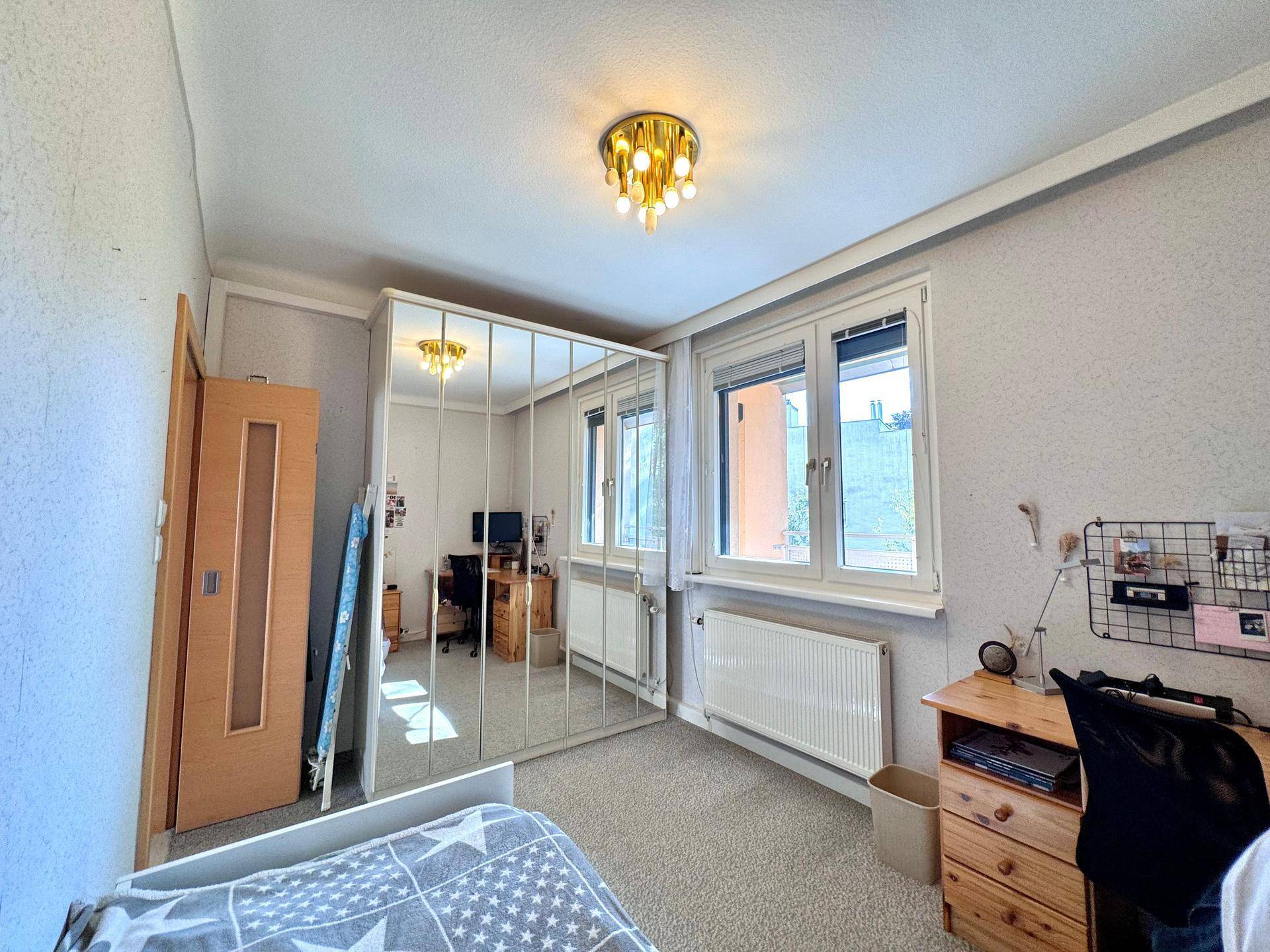 Schlafzimmer mit großem Spiegelschrank, Einzelbett und Schreibtisch.