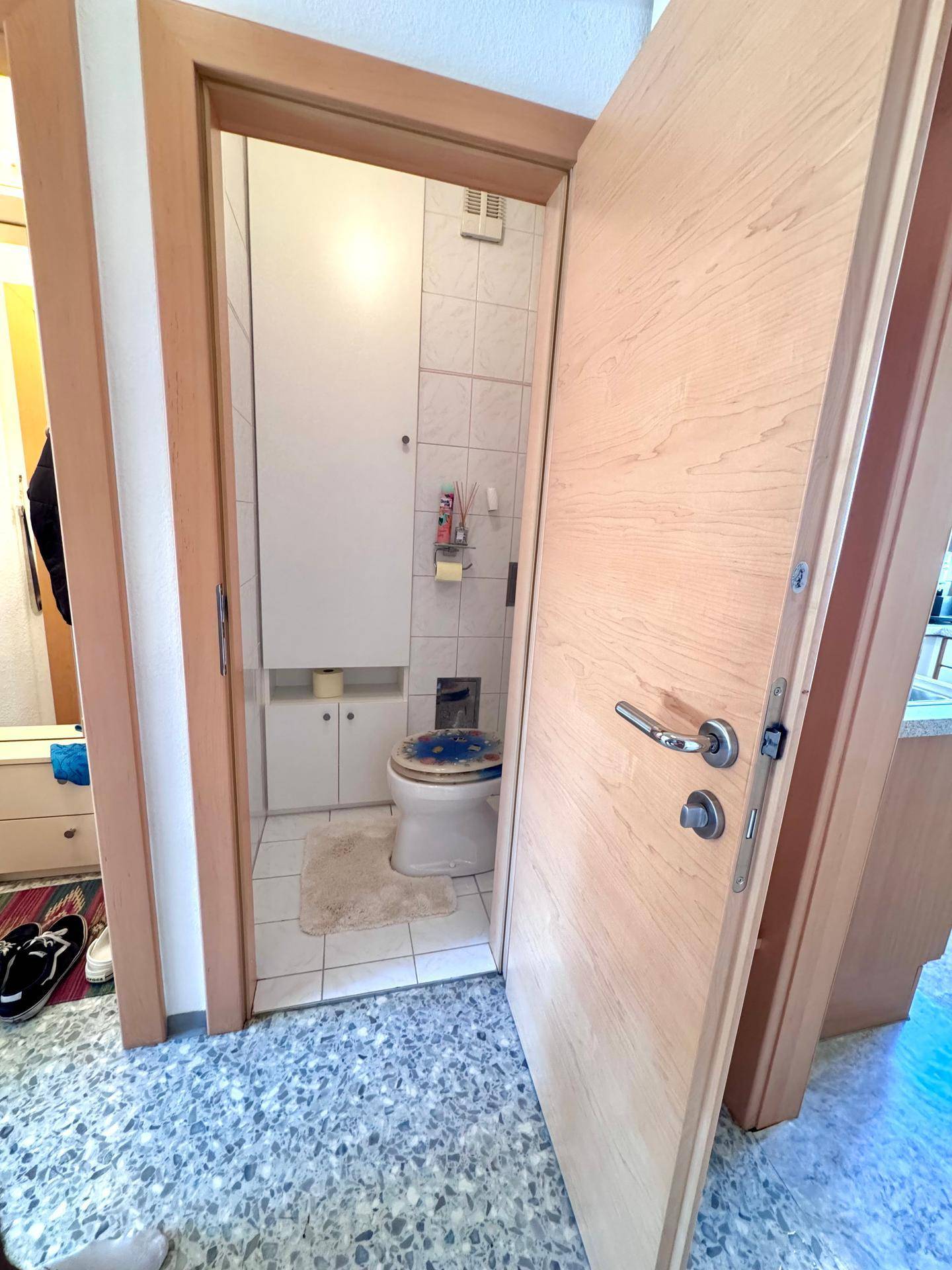 Separates Gäste-WC mit Toilette und kleinem Waschbecken, durch eine offene Tür sichtbar.