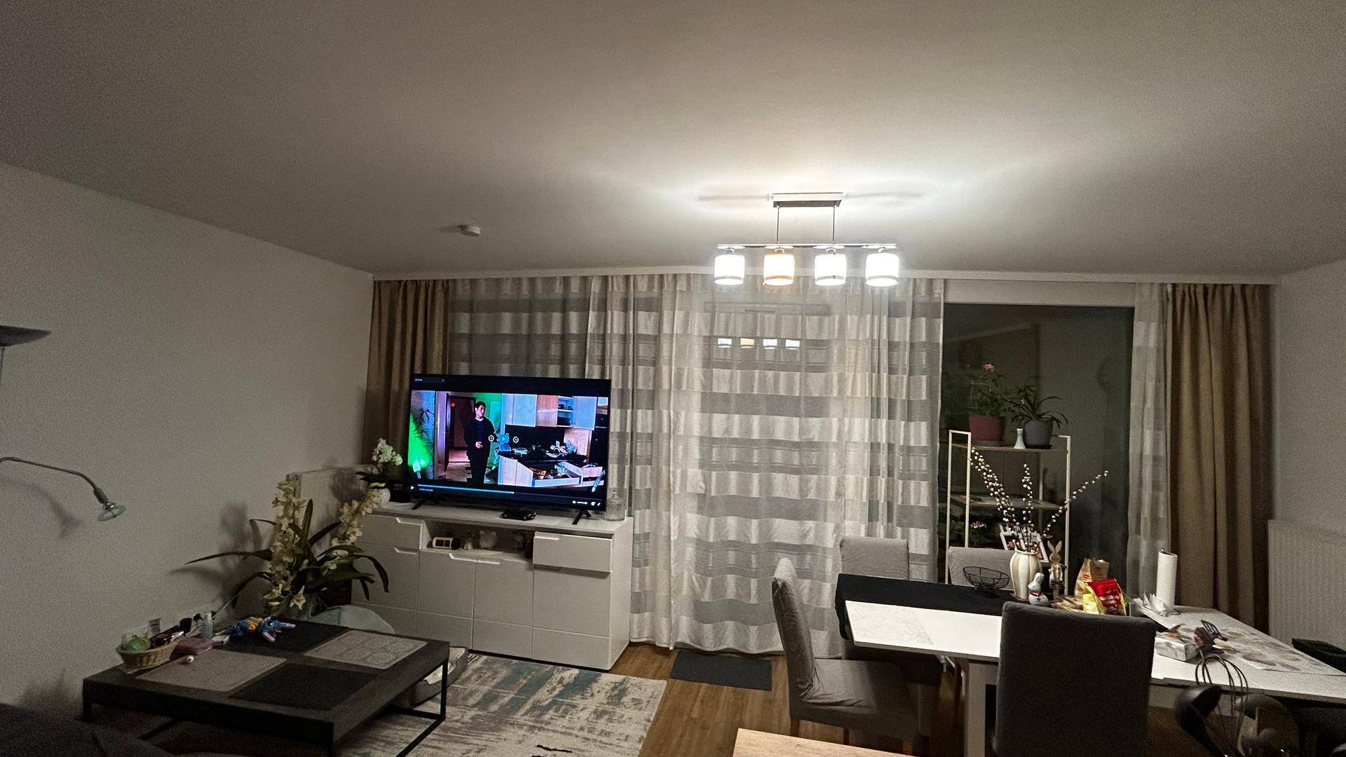 Gemütlicher Wohn-Essbereich mit Fernseher, Esstisch und Zugang zu einem Balkon oder einer Terrasse.