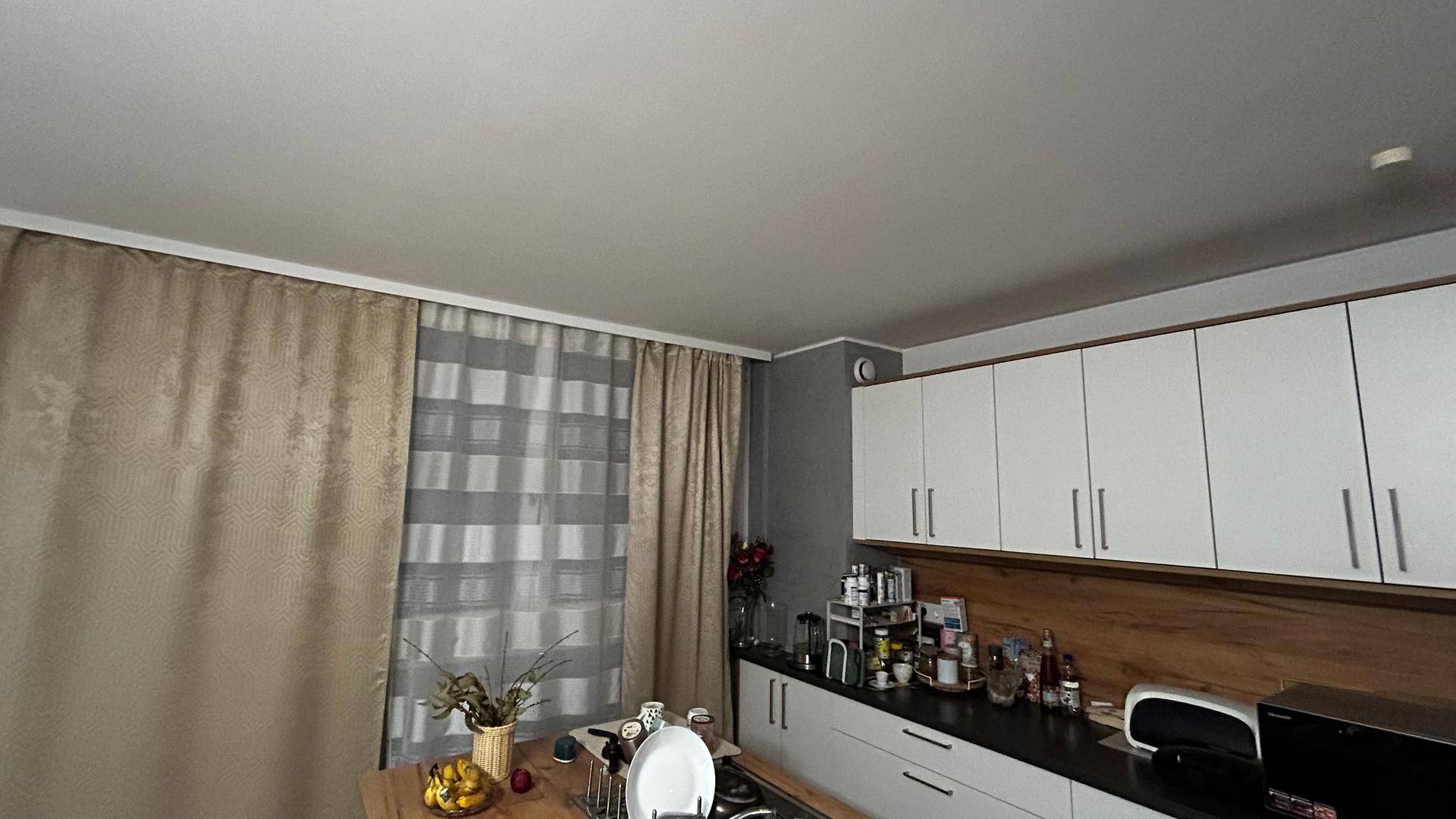 Moderne Küche mit weißen Oberschränken, Holzrückwand und einem Fenster mit Vorhängen.