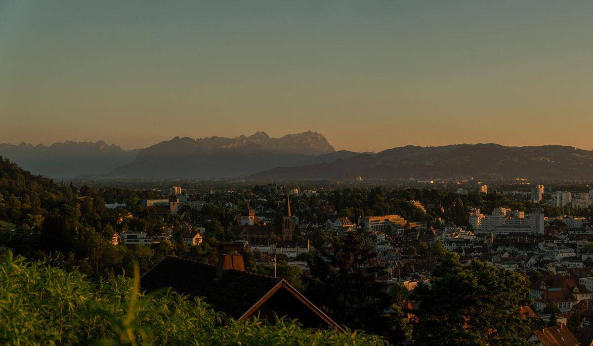 Weitläufiger Blick über die Stadt und die majestätischen Berge in der Ferne bei Dämmerung.