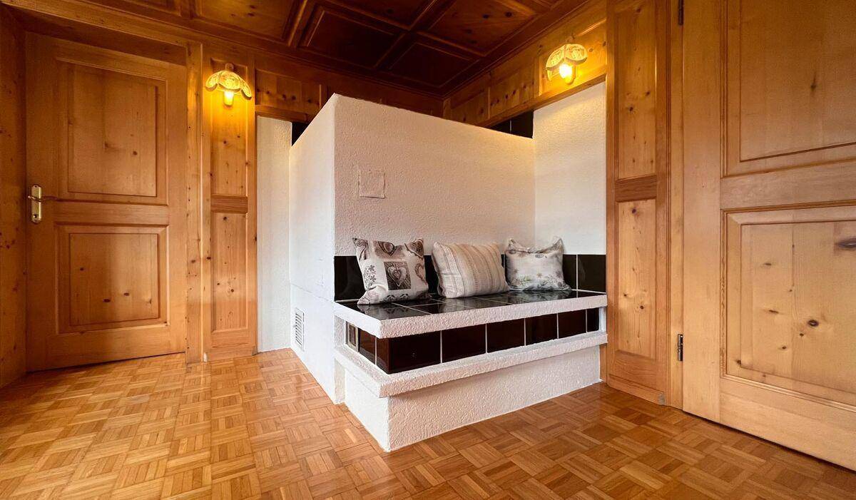 Detailansicht des traditionellen Kachelofens mit Sitzbank und Holztäfelung im Wohnbereich.