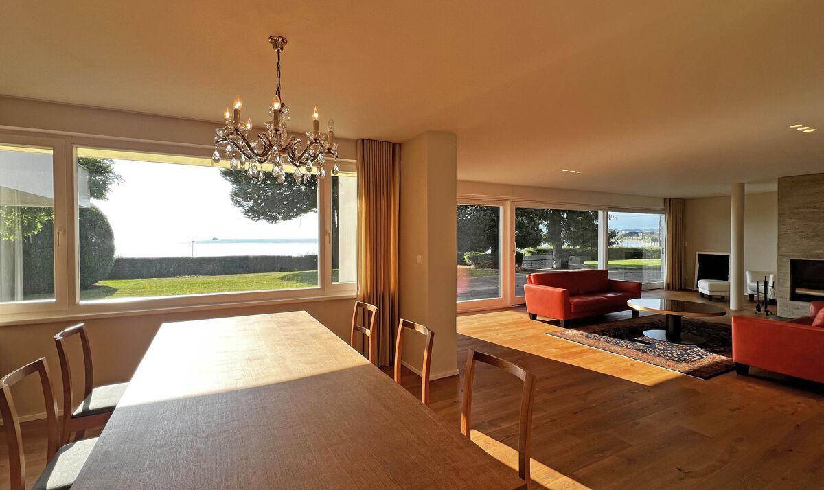 Lichtdurchfluteter Wohn- und Essbereich mit Kronleuchter, Holzboden und Panoramablick auf den See.