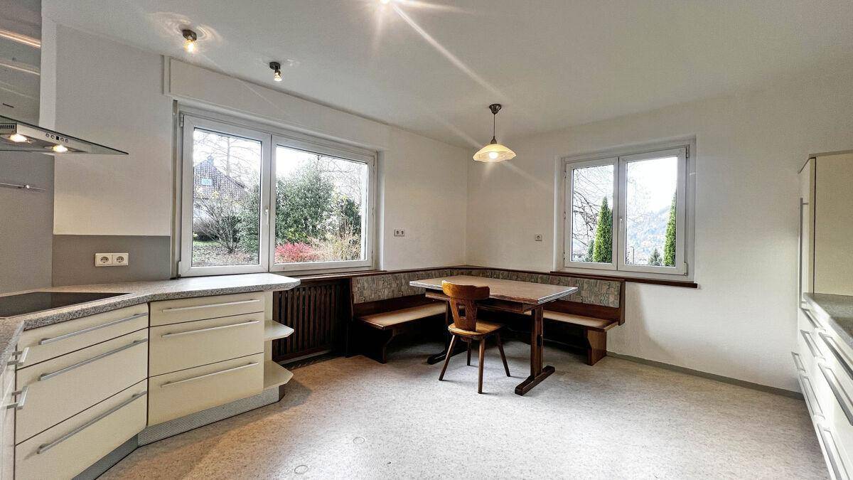 Gemütlicher Essbereich in der Küche mit Sitzbank und Blick ins Grüne durch große Fenster.