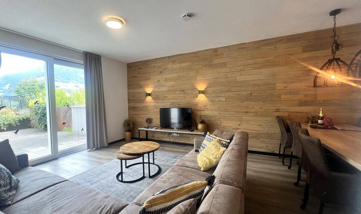 Heller Wohnbereich mit großem Sofa, Fernseher und Zugang zur Außenterrasse.