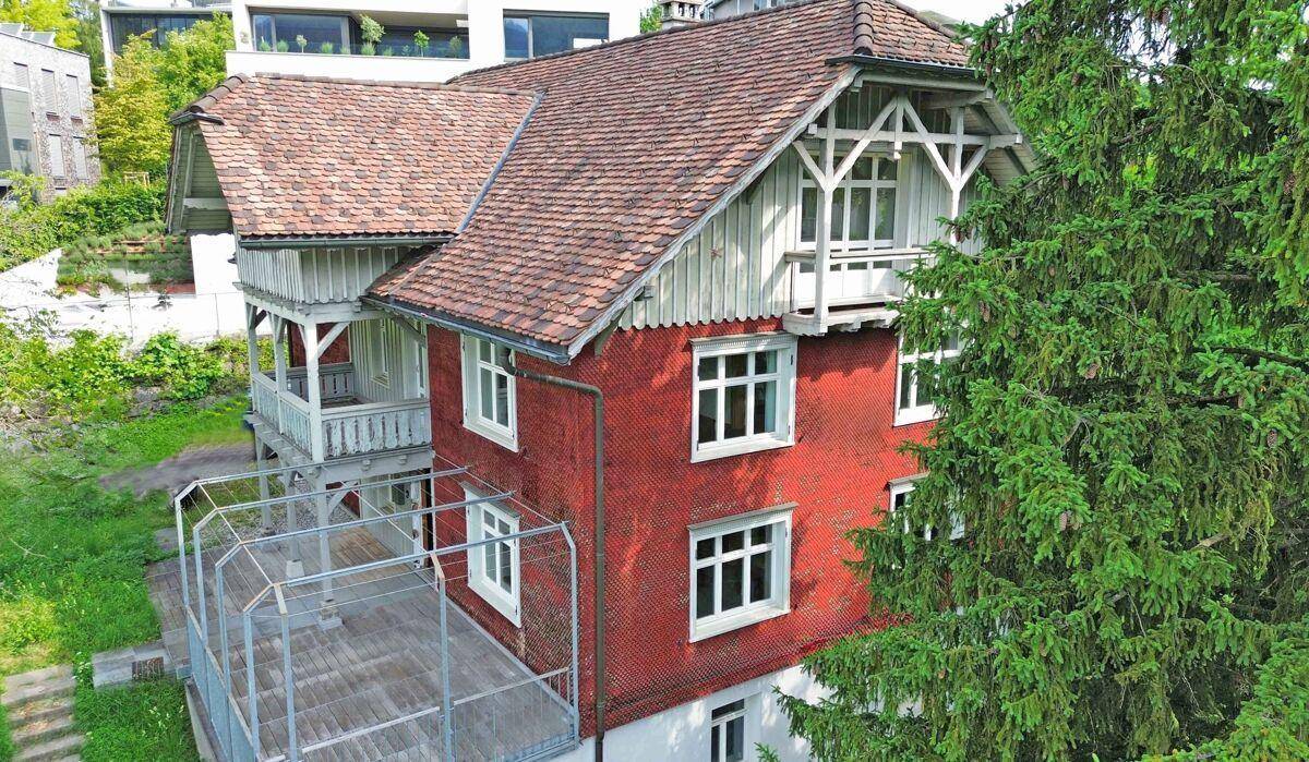 Vogelperspektive eines traditionellen Hauses mit roter Fassade, Holzbalkonen und einem Gartenbereich.