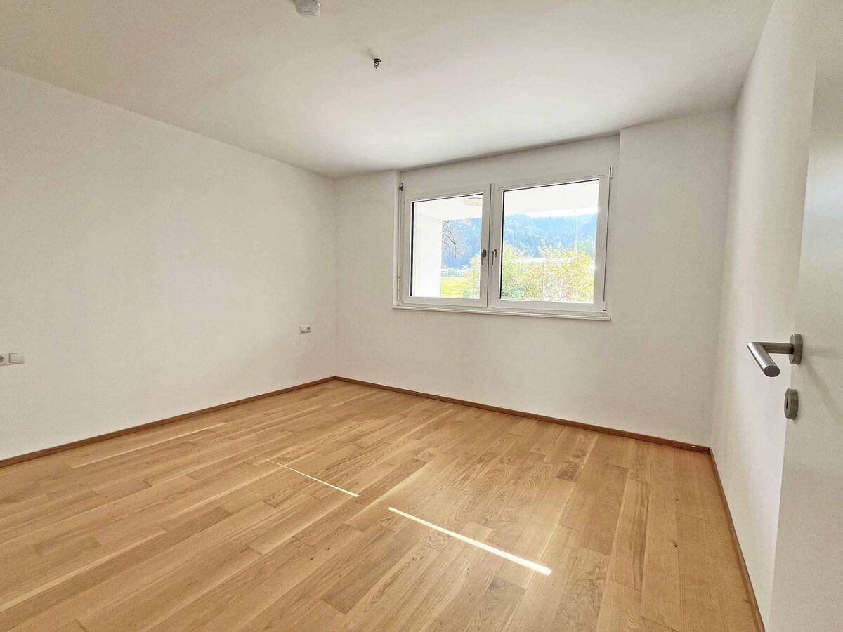 Helles Schlafzimmer mit Holzboden und großen Fenstern, die viel Tageslicht hereinlassen.