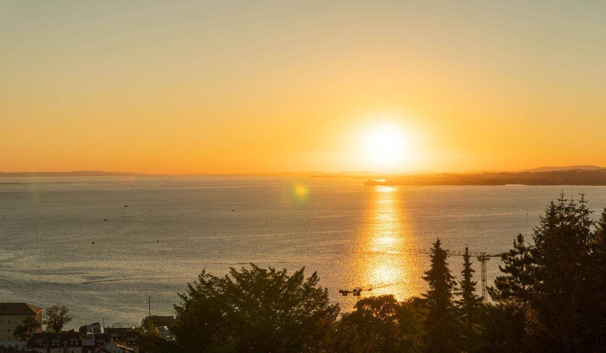 Strahlender Sonnenuntergang über dem See mit intensiver Lichtreflexion auf der Wasseroberfläche.