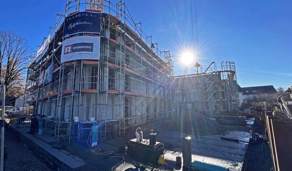 Baustelle eines Neubaus mit Gerüst und Baukran, die Sonne scheint hell auf das Gebäude.