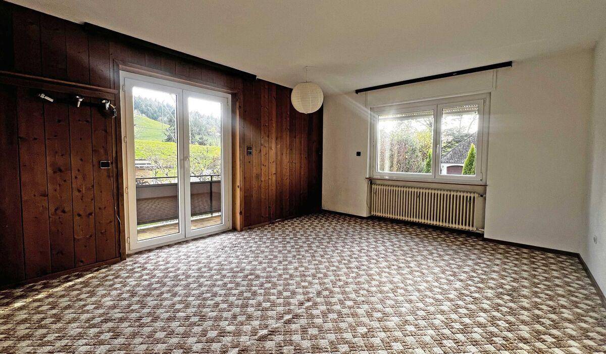 Wohnraum mit gemustertem Teppich, Holzwänden und Zugang zu einem Balkon.