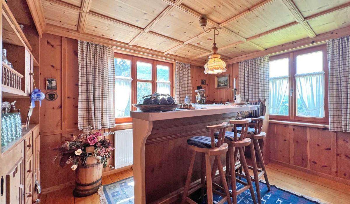 Gemütliche Bar im Alpenstil mit Holztäfelung, Hockern und Blick auf die grüne Umgebung.