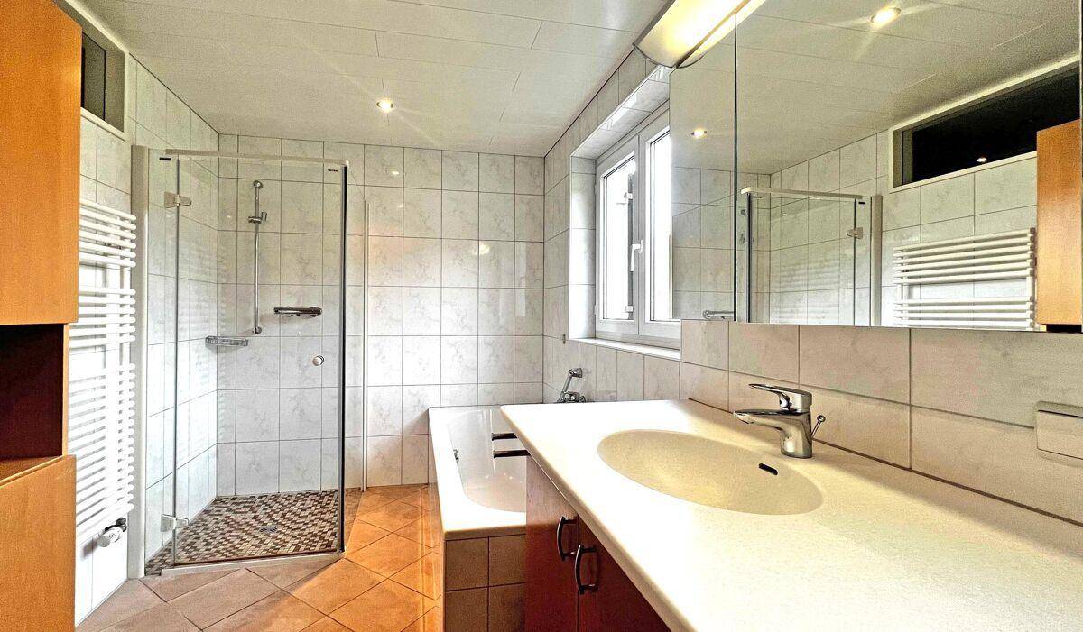 Helles Badezimmer mit Dusche, Badewanne, Fenster und weiß gefliesten Wänden.