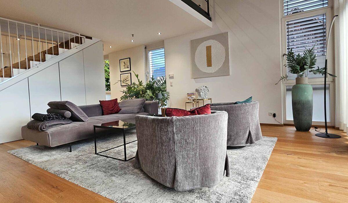 Helles Wohnzimmer mit großem Sofa, Sesseln, Couchtisch und Holzfußboden, offen gestaltet mit Treppenaufgang.