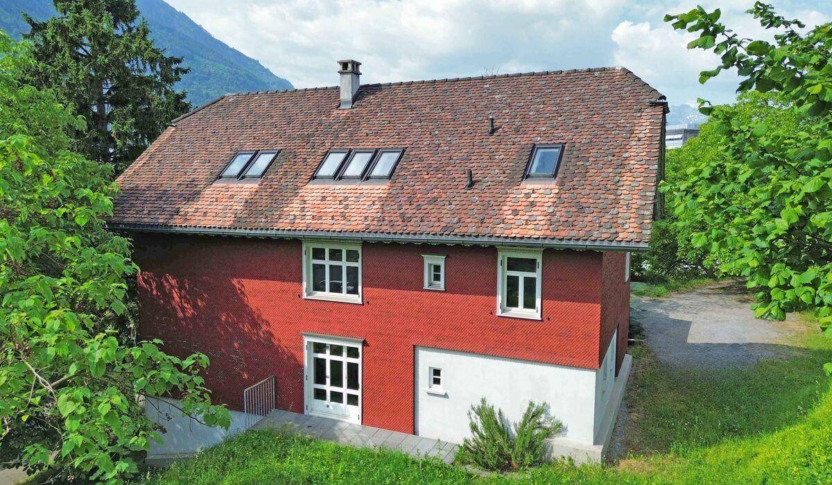 Rückseite des Hauses mit roter Fassade, Dachfenstern und Zugang zum Gartenbereich.