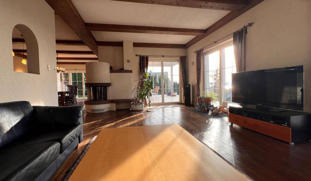 Helles Wohnzimmer mit Holzbalken, Kamin und Zugang zur Terrasse mit viel Tageslicht.