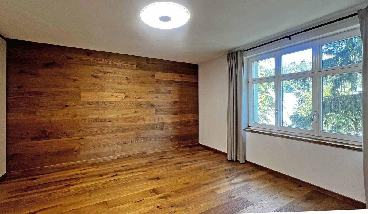 Modernisiertes Schlafzimmer mit Holzwand, neuem Holzboden und großen Fenstern.
