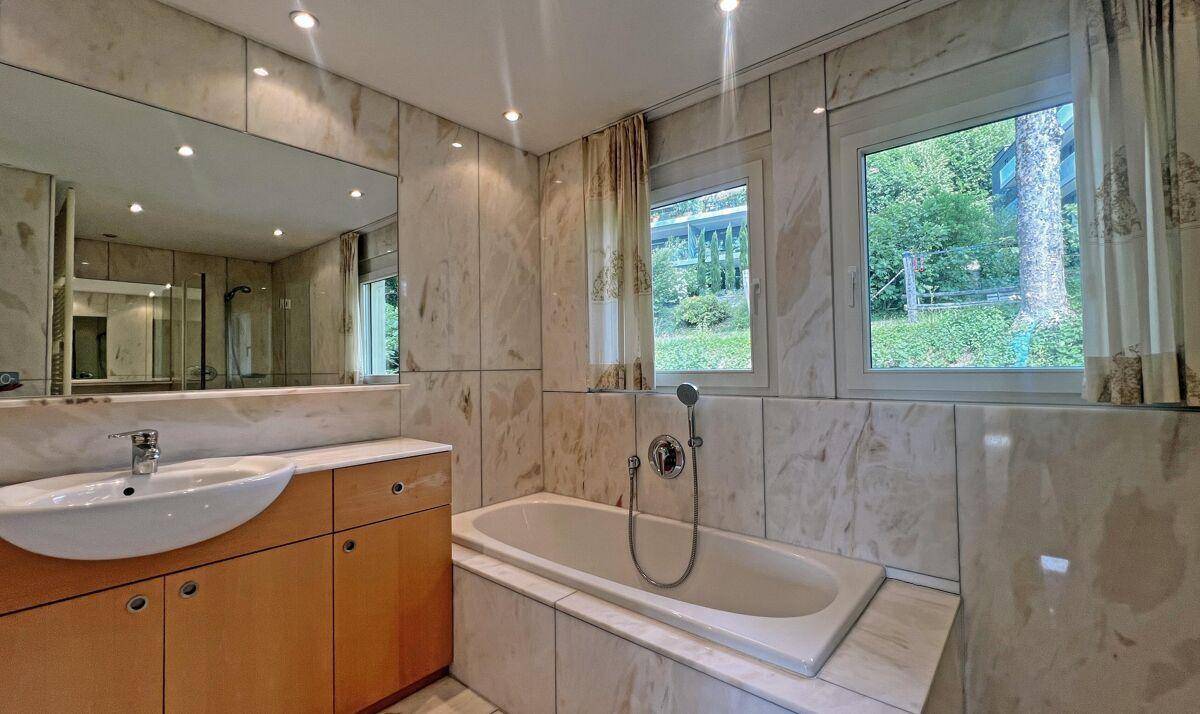 Elegantes Badezimmer mit Badewanne, Einzelwaschbecken und Fenster, umgeben von Marmorfliesen.