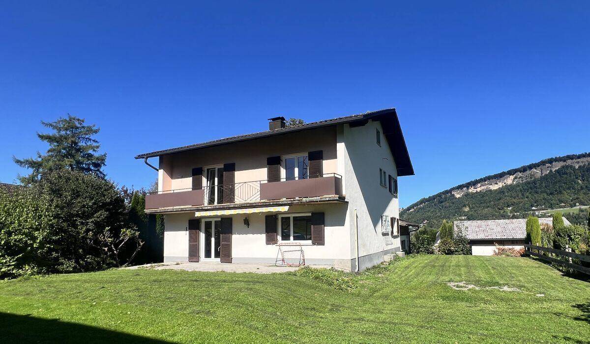 Das Einfamilienhaus im Sommer mit grünem Rasen und Blick auf die umliegende Berglandschaft.