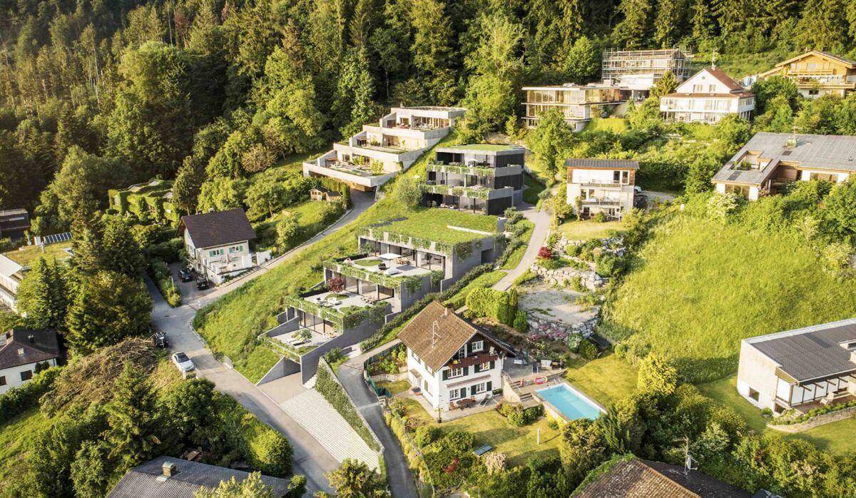 Luftaufnahme einer modernen Wohnanlage, die sich terrassenförmig in die grüne Hügellandschaft einfügt, umgeben von Natur.