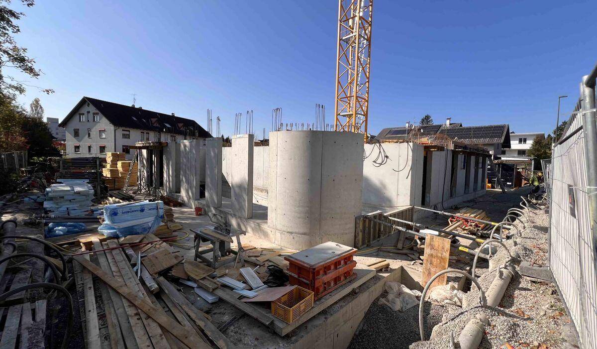 Baustelle mit bereits errichteten Betonwänden des Erdgeschosses und Baukran.