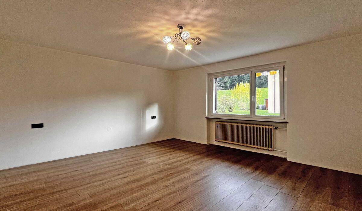 Heller, leerer Raum mit neuem Holzfußboden und einem großen Fenster mit Blick ins Grüne.