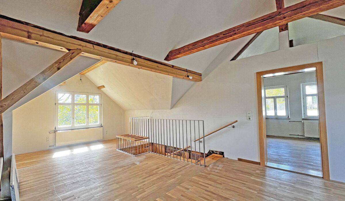 Ausgebauter Dachboden mit sichtbaren Holzbalken und hellem Parkettboden.