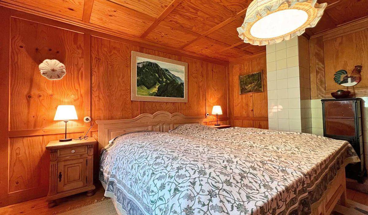 Schlafzimmer im traditionellen Stil mit Holztäfelung, Doppelbett und einem Kachelofen.