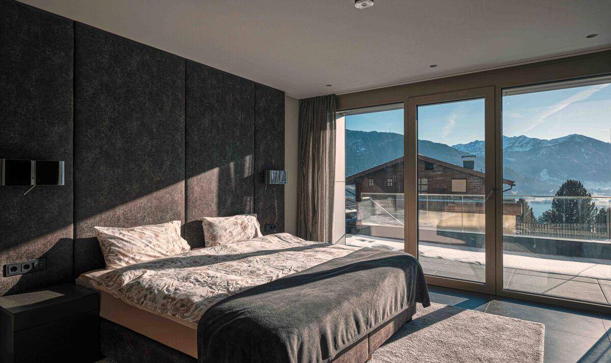 Elegantes Schlafzimmer mit gepolsterter Wand, großen Fenstern und weitem Blick auf die umliegende Landschaft.