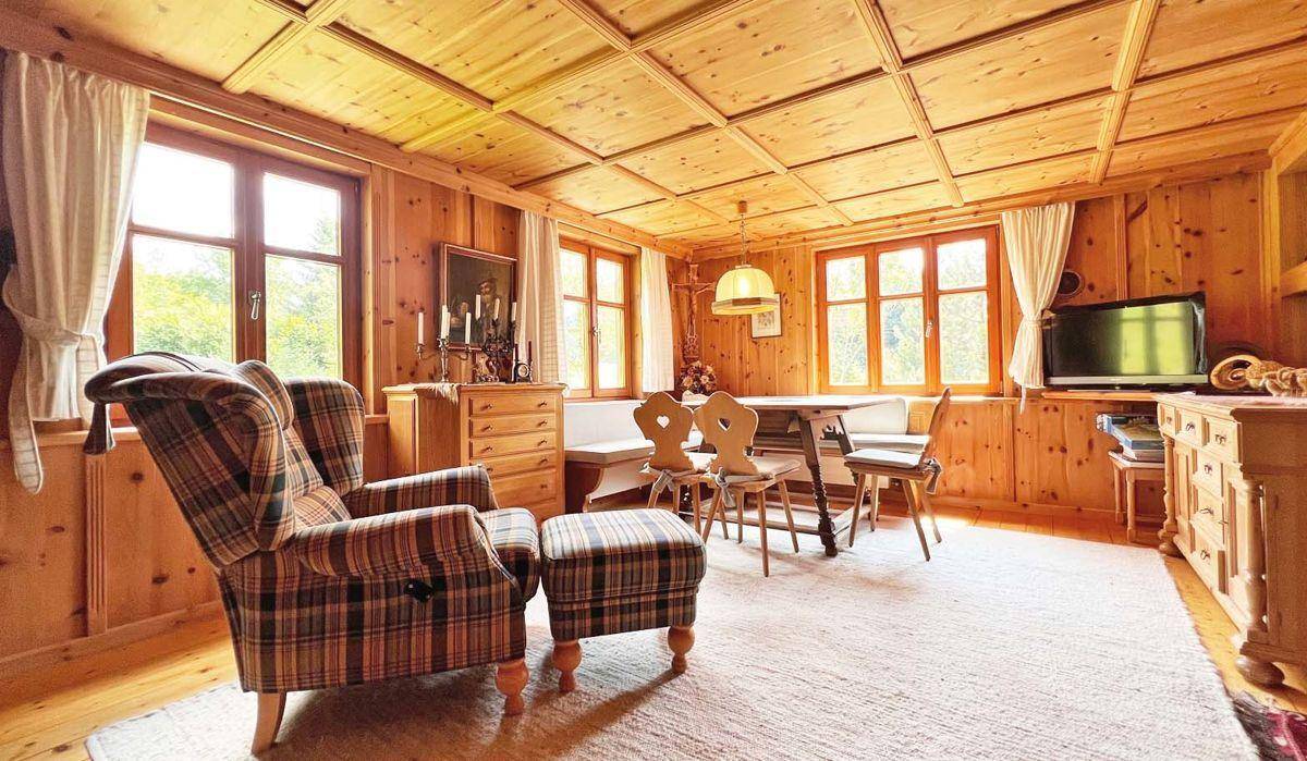 Helles Wohnzimmer im Alpenstil mit kariertem Sessel, Holztäfelung und Essbereich im Hintergrund.