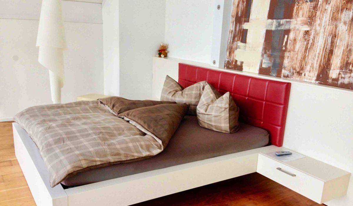 Gemütliches Schlafzimmer mit Doppelbett, rotem Kopfteil und Holzboden.