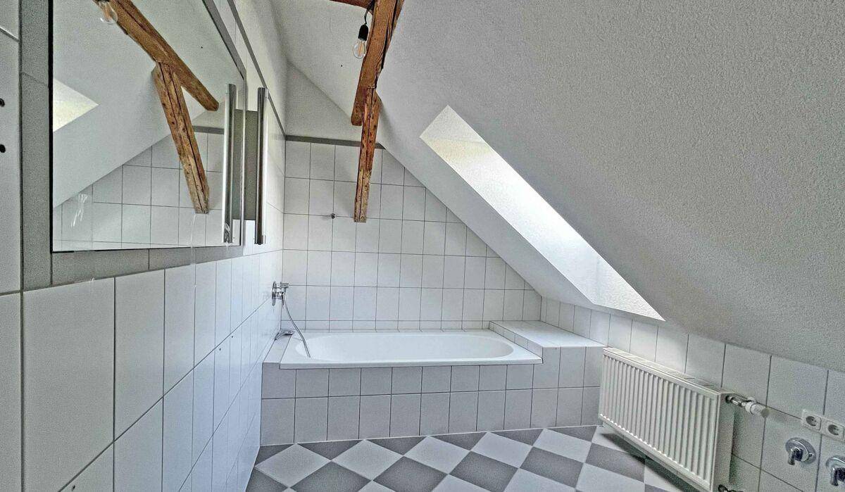 Dachgeschoss-Badezimmer mit Badewanne, weißen Fliesen und schräger Decke.