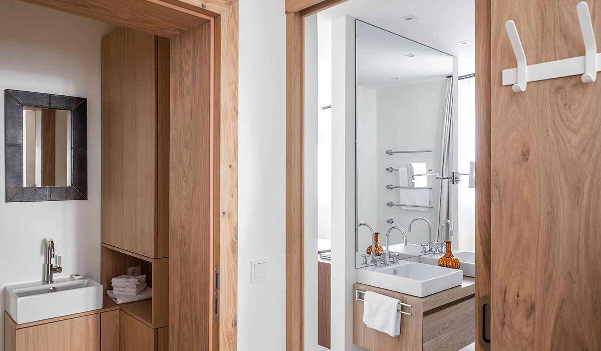 Flur mit Holztüren und Blick in ein modernes Badezimmer mit Doppelwaschbecken.