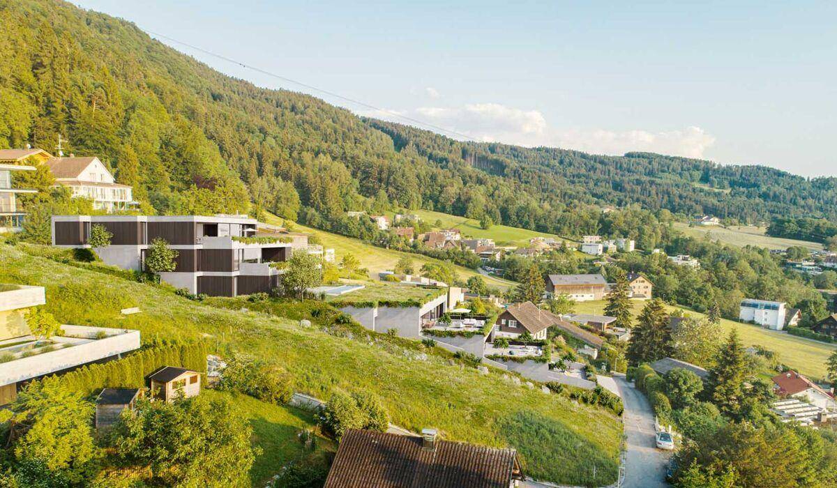 Weitläufige Ansicht der terrassierten Wohngebäude, eingebettet in die grüne Hügellandschaft mit Blick auf die Umgebung.