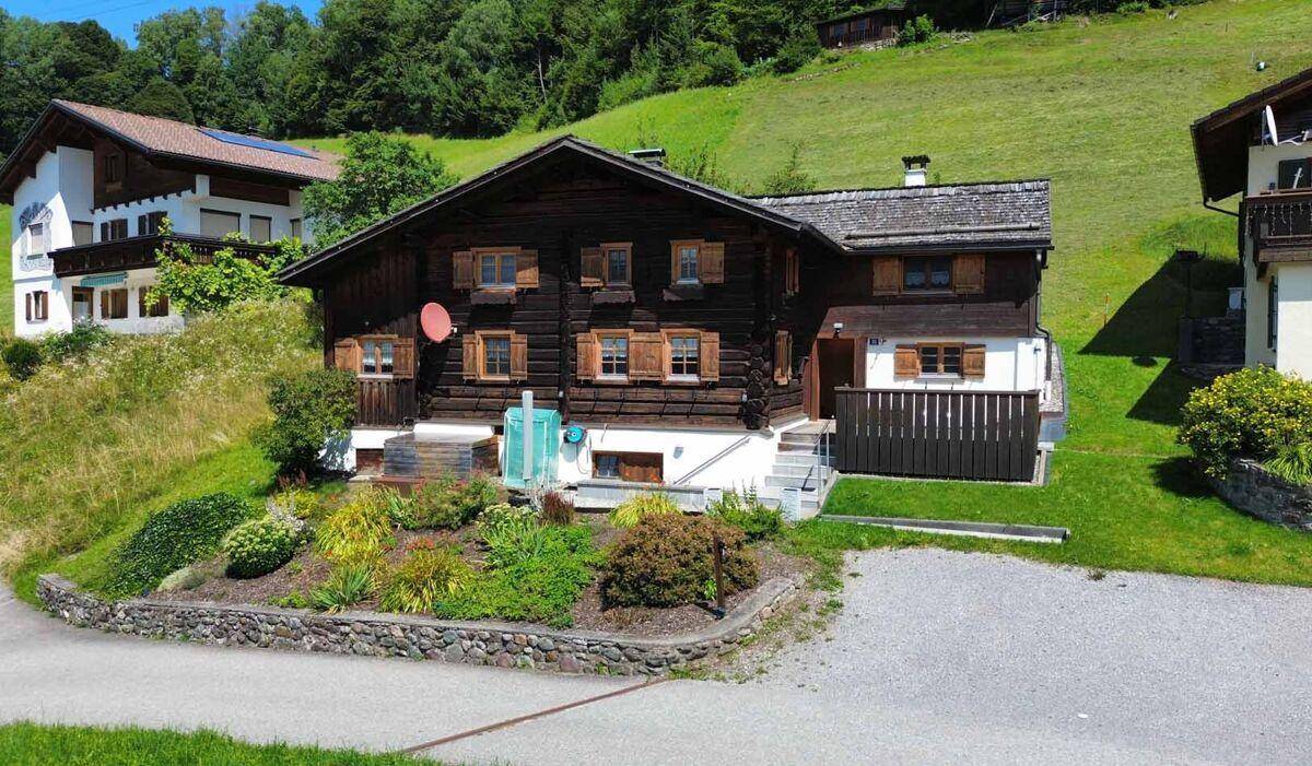Traditionelles Holzhaus im alpinen Stil mit gepflegtem Vorgarten und grüner Umgebung.