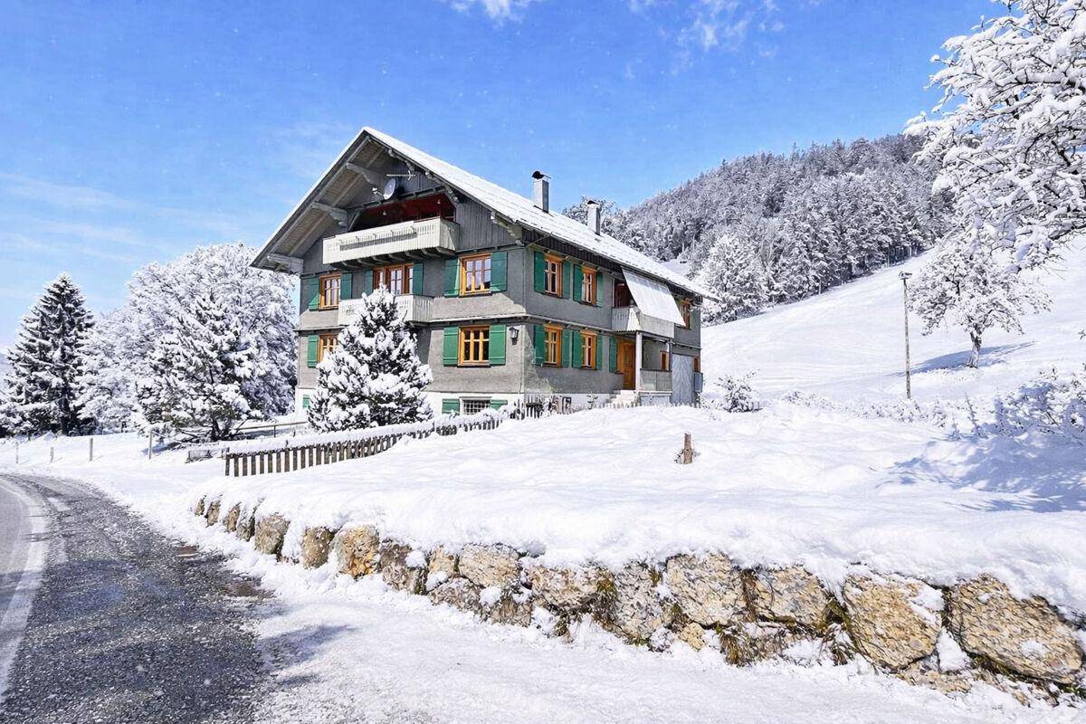 Idyllisches Haus in verschneiter Berglandschaft mit grünen Fensterläden und Balkon.