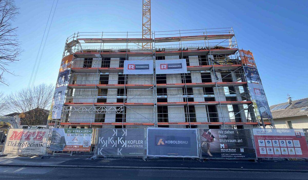 Gebäude im Bau mit Gerüst und Kran, umgeben von Werbebannern für neue Wohnungen.