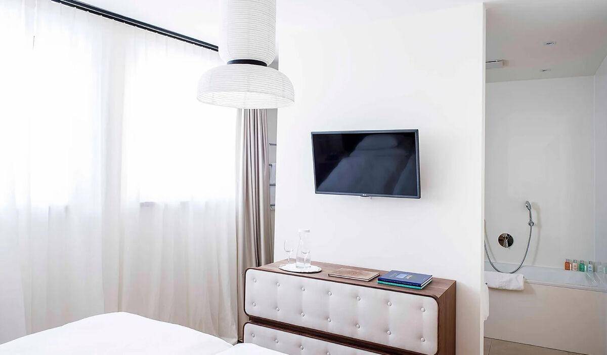 Schlafzimmer mit Wandfernseher, moderner Kommode und angrenzendem Badezimmerbereich.