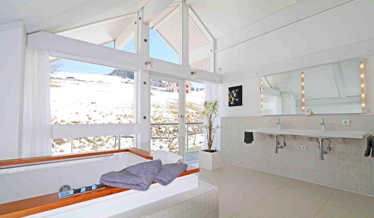 Großes, helles Badezimmer mit Doppelwaschbecken, Badewanne und Panoramablick auf die verschneite Landschaft.