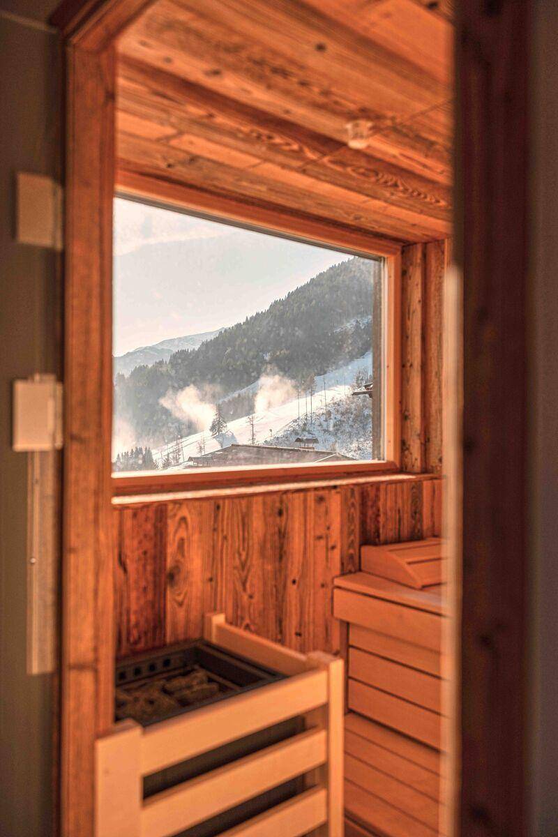 Gemütliche Sauna mit Holzverkleidung und Fensterblick auf die verschneite Berglandschaft.