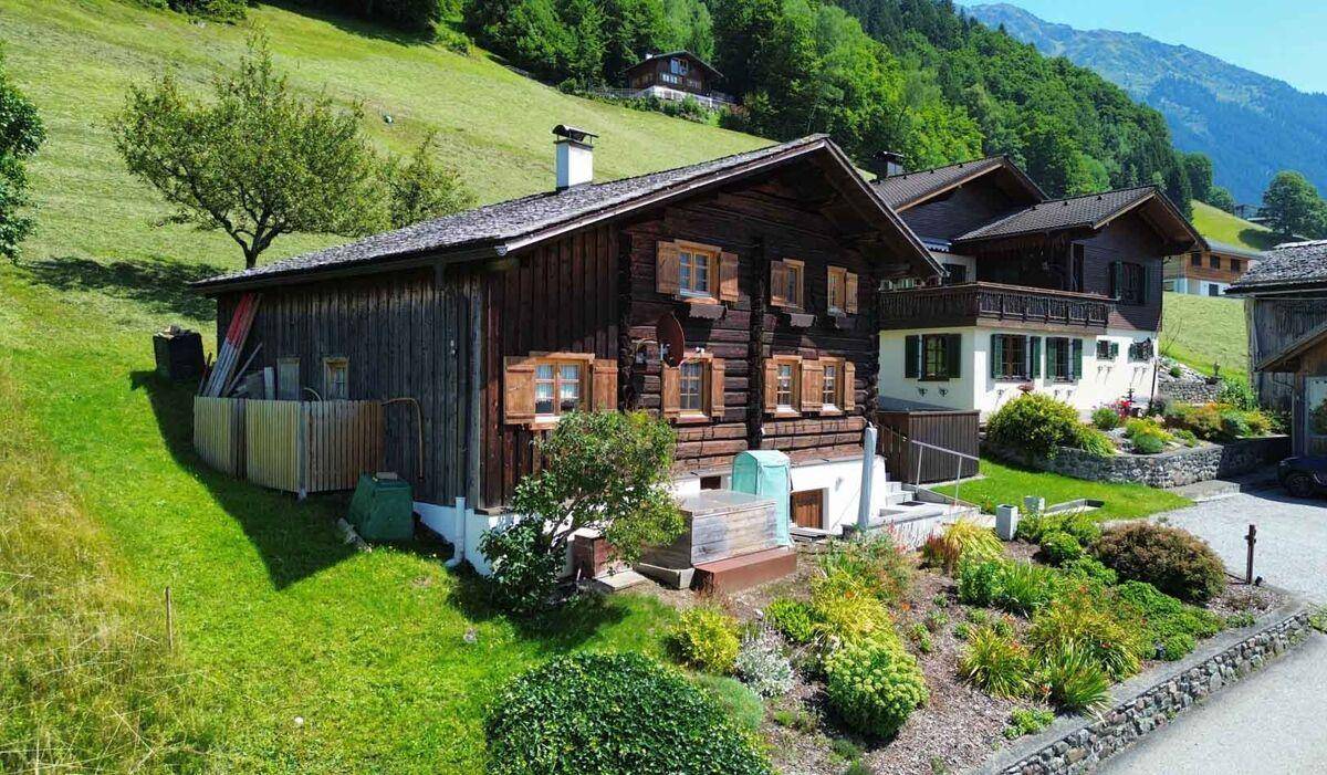 Seitenansicht des Holzhauses mit Garten und angrenzendem Hang in sonniger Lage.