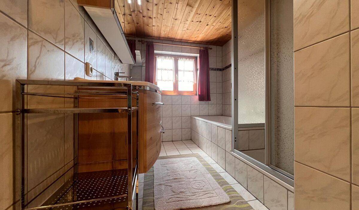 Badezimmer mit Fliesen, Badewanne und Duschkabine sowie Holzdecke.