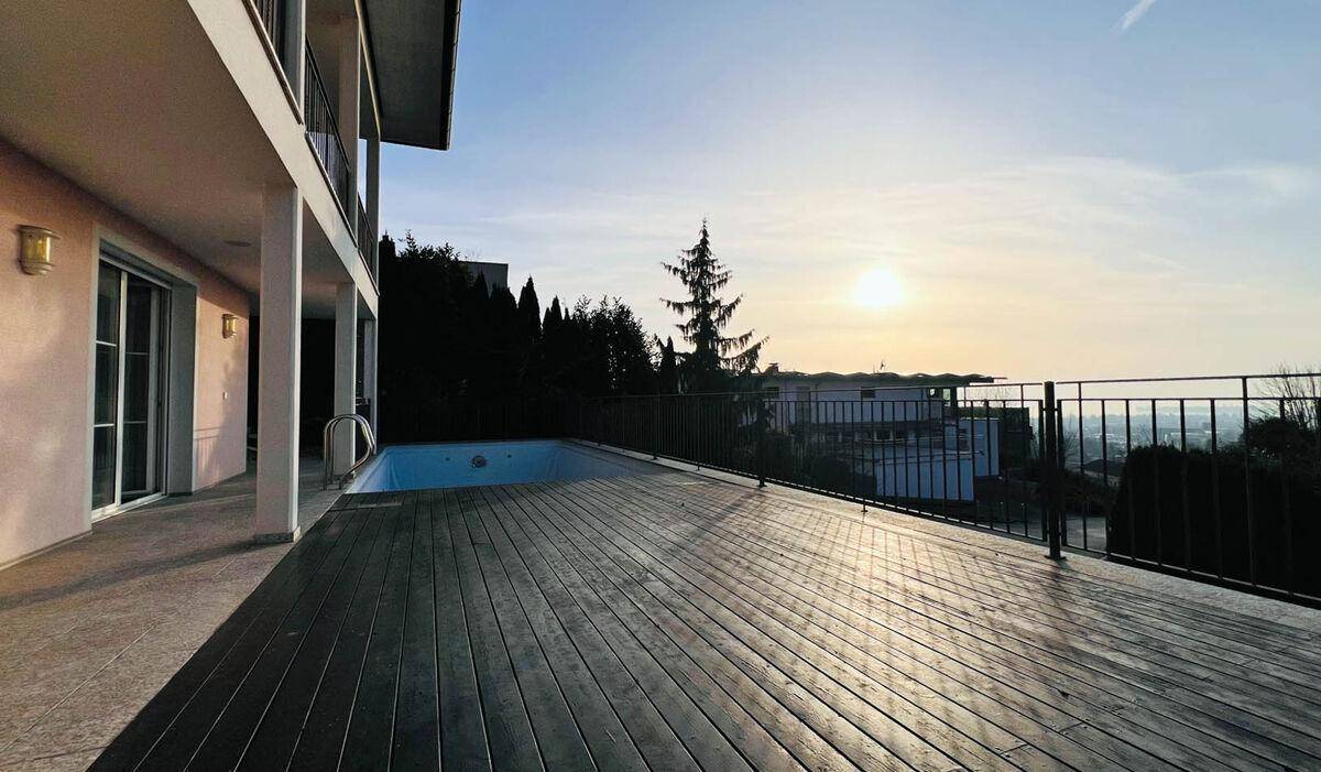 Große Holzterrasse mit Pool und weitem Blick in die Ferne bei Sonnenuntergang.