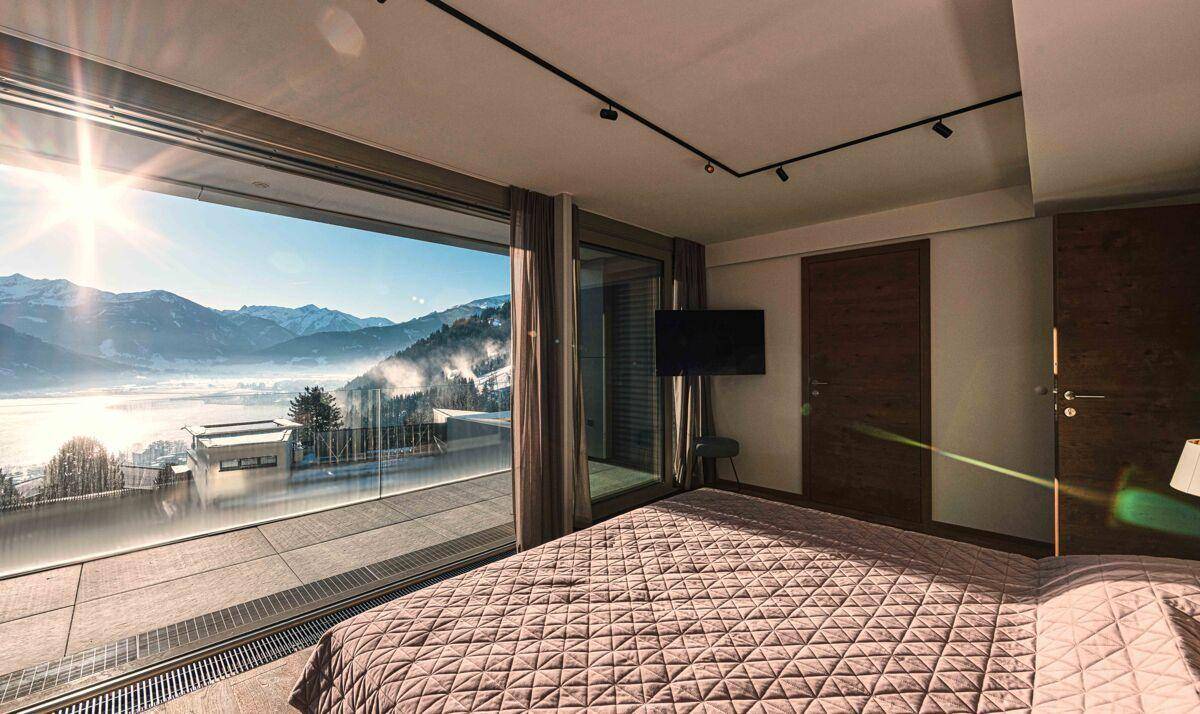 Helles Schlafzimmer mit großen Fenstern, direktem Zugang zur Terrasse und Panoramablick auf den See und die Berge.