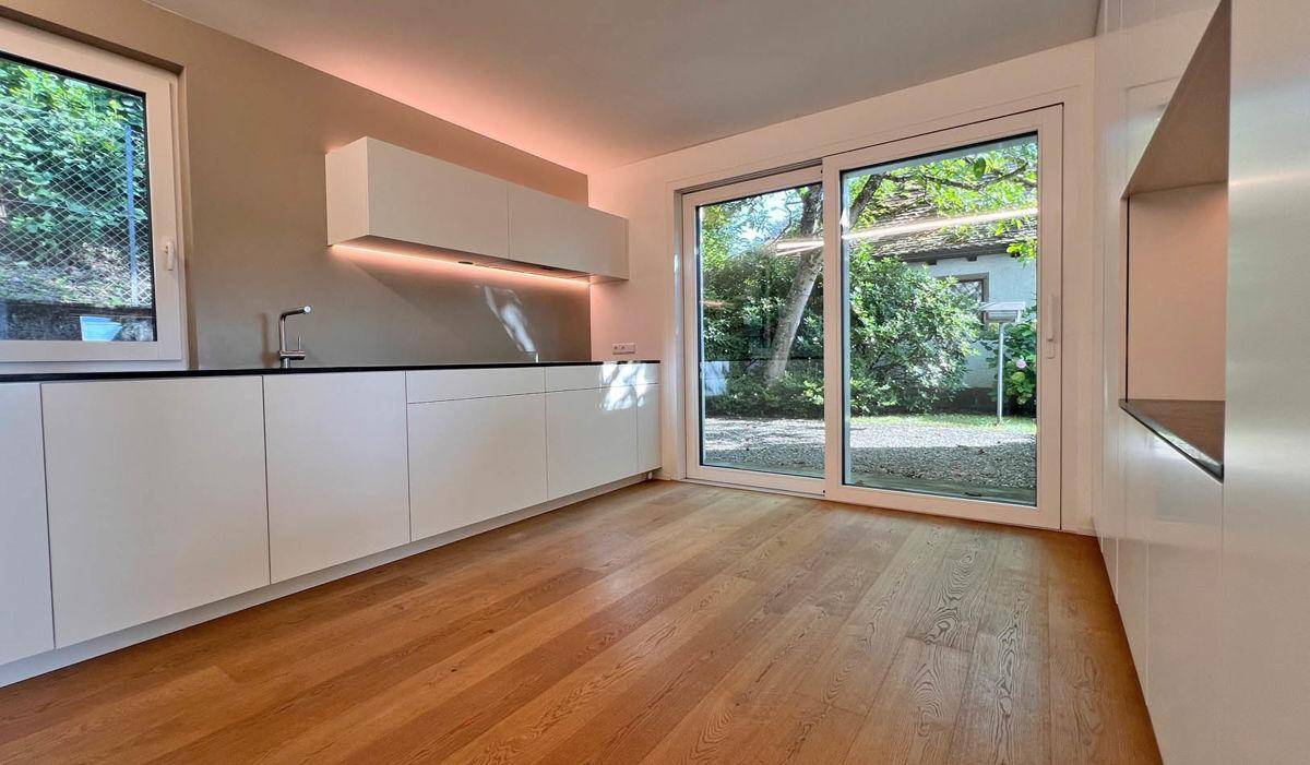 Moderne Einbauküche mit weißen Schränken, Holzboden und direktem Zugang zum Garten.