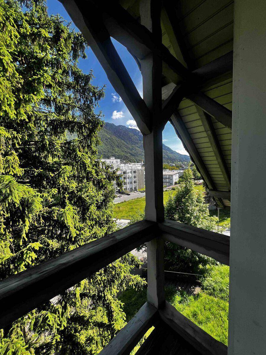 Kleiner Holzbalkon mit Bergblick, umgeben von grünen Bäumen.