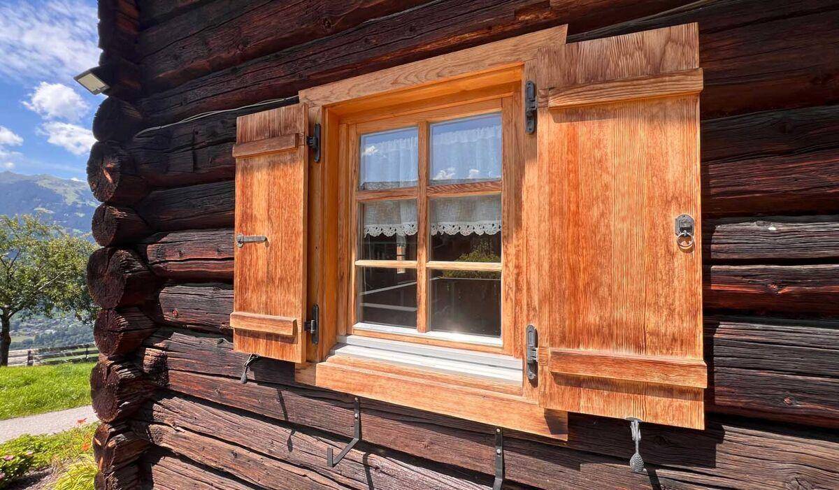 Nahaufnahme eines Holzfensters mit traditionellen Fensterläden an der Blockhausfassade.
